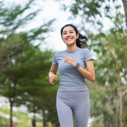 Happy slim woman wearing sportswear jogging in the city at sunrise. Young beautiful asian female in sports bra running outdoor. Workout exercise in the morning. Healthy and active lifestyle concept.